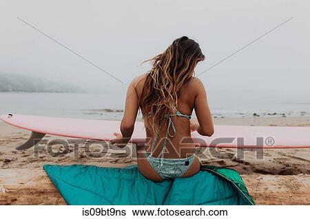 Young female surfer sitting on log looking at surfboard on beach, rear view, Ventura, California, USA View Large Photo Image Stock Photograph - Young female surfer sitting on log looking at surfboard on beach, rear view, Ventura, California, USA. Fotosearch