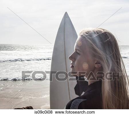 Stock Photo - Young female surfer with surfboard gazing on beach, Cape Town, Western Cape, South Africa. Fotosearch