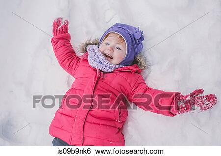 Stock Photograph - Young girl making snow angel in snow, close-up. Fotosearch