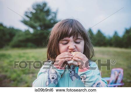Stock Photograph - Young girl, outdoors, eating s'more, close-up. Fotosearch