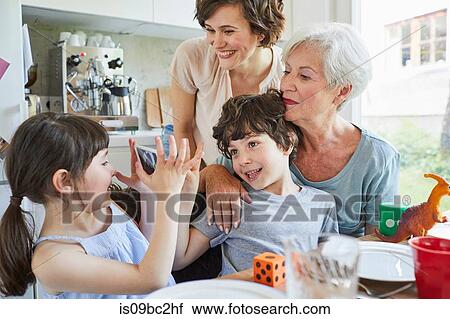 Stock Image - Young girl photographing, brother, mother and grandmother, using smartphone. Fotosearch