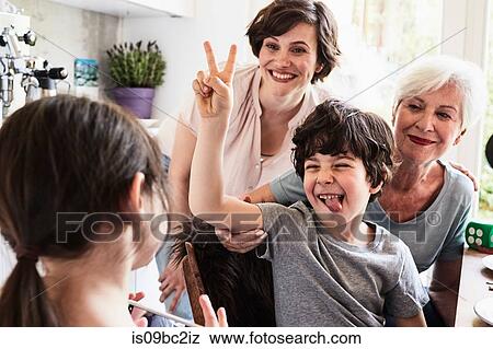 Stock Photo - Young girl photographing, brother, mother and grandmother, using smartphone. Fotosearch