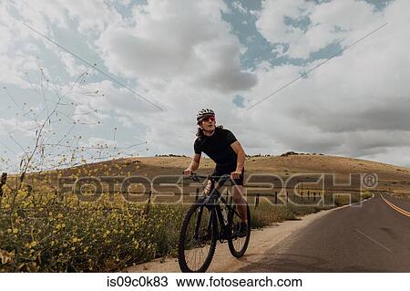 Young male cyclist looking away while cycling on rural road, Exeter, California, USA View Large Photo Image Stock Image - Young male cyclist looking away while cycling on rural road, Exeter, California, USA. Fotosearch