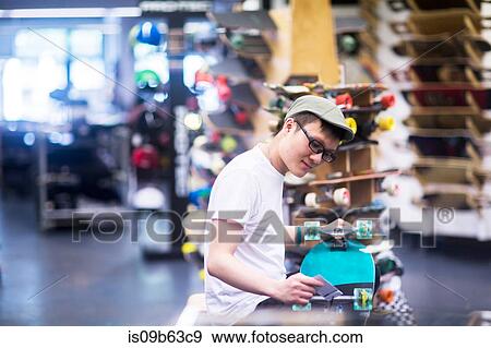 Stock Photo - Young male sales assistant repairing skateboard at skateboard shop counter. Fotosearch