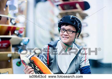 Stock Image - Young male skateboarder holding skateboard in skateboard shop. Fotosearch