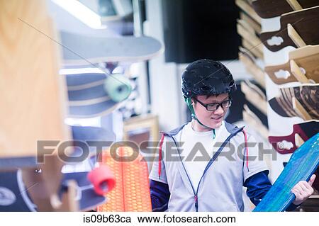 Stock Image - Young male skateboarder looking at skateboards in skateboard shop. Fotosearch