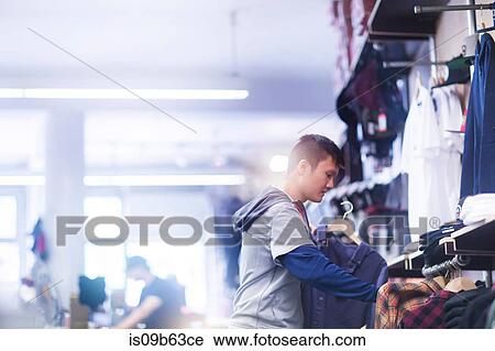 Young male skateboarder looking at shirt in skateboard shop View Large Photo Image Stock Image - Young male skateboarder looking at shirt in skateboard shop. Fotosearch