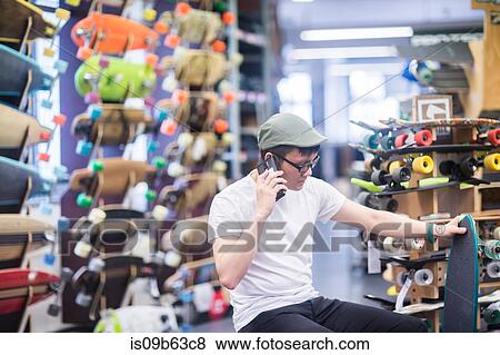 Stock Photo - Young male skateboarder making smartphone call in skateboard shop. Fotosearch