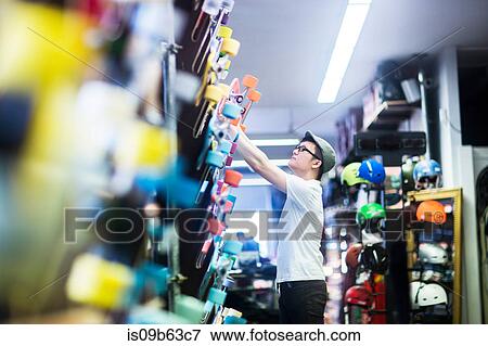 Young male skateboarder removing skateboard from wall in skateboard shop View Large Photo Image Stock Photo - Young male skateboarder removing skateboard from wall in skateboard shop. Fotosearch