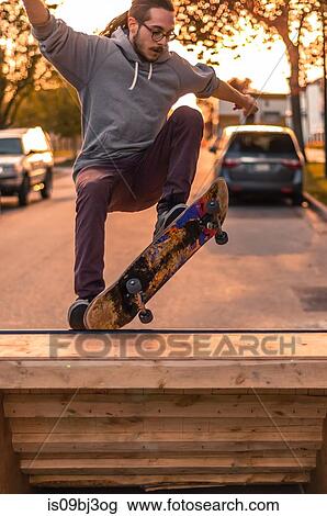 Stock Image - Young male skateboarder turning on top of ramp on suburban street at sunset. Fotosearch