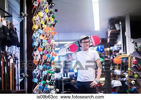 Young male skateboarder with skateboard over his shoulder in skateboard shop View Large Photo Image Stock Image - Young male skateboarder with skateboard over his shoulder in skateboard shop. Fotosearch