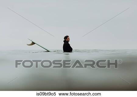 Stock Photography - Young male surfer by surfboard in misty sea, Ventura, California, USA. Fotosearch
