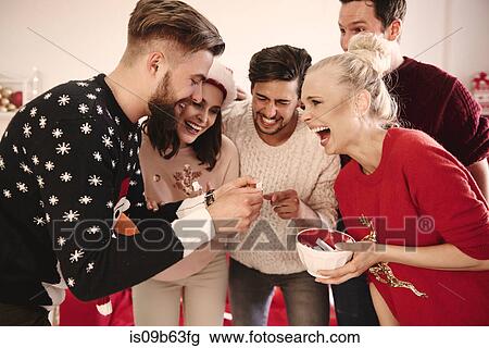 Stock Image - Young man and friends reading fortune message at christmas party. Fotosearch