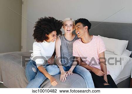 Young man and two female friends sitting on bed laughing together View Large Photo Image Stock Image - Young man and two female friends sitting on bed laughing together. Fotosearch