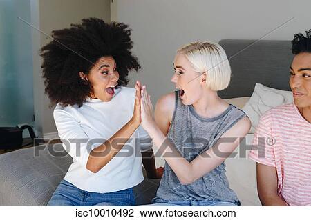 Young man and two female friends sitting on bed high fiving View Large Photo Image Stock Image - Young man and two female friends sitting on bed high fiving. Fotosearch
