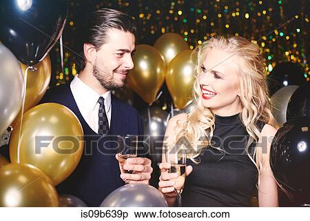 Stock Photography - Young man and woman at party, holding champagne glasses, smiling. Fotosearch