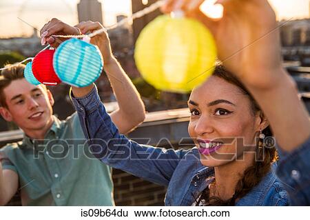 Stock Photograph - Young man and woman hanging lights at roof party in London, UK. Fotosearch