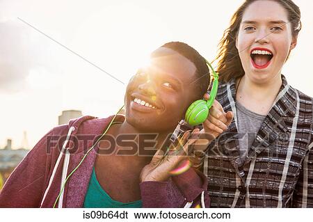 Young man and woman listening to headphone music at roof party in London, UK View Large Photo Image Stock Photograph - Young man and woman listening to headphone music at roof party in London, UK. Fotosearch