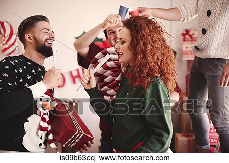 Stock Photography - Young man and woman singing with pretend microphones at christmas party. Fotosearch