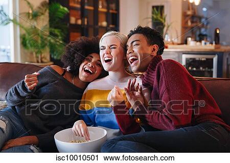 Young man and young female friends laughing while watching tv on living room sofa with bowl of popcorn View Large Photo Image Stock Image - Young man and young female friends laughing while watching tv on living room sofa with bowl of popcorn. Fotosearch