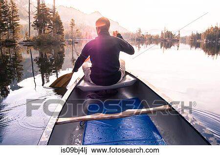 Stock Image - Young man canoeing on Echo Lake, rear view, High Sierras, California, USA. Fotosearch