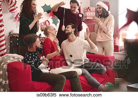Stock Photography - Young man eating dangled doughnut at christmas party. Fotosearch