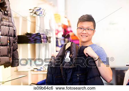 Young man holding jacket in clothes shop View Large Photo Image Stock Photograph - Young man holding jacket in clothes shop. Fotosearch