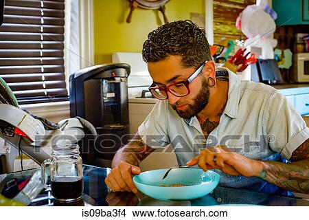Young man in spectacles eating at kitchen table View Large Photo Image Picture - Young man in spectacles eating at kitchen table. Fotosearch