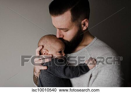 Stock Image - Young man kissing baby son on head, head and shoulders. Fotosearch