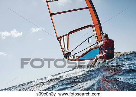 Stock Photo - Young man leaning back windsurfing ocean waves, angled view, Limnos, Khios, Greece. Fotosearch