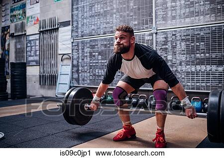 Stock Image - Young man lifting barbell in gym. Fotosearch