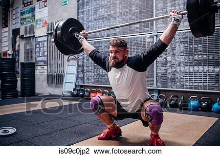 Stock Image - Young man lifting barbell in gym. Fotosearch
