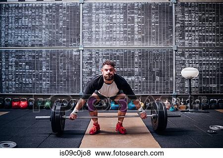 Stock Photo - Young man lifting barbell in gym. Fotosearch