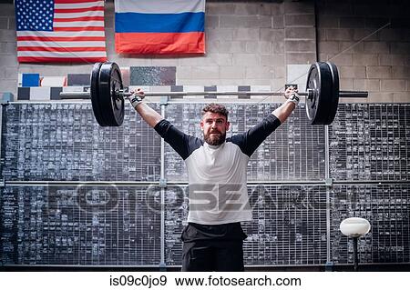 Stock Photo - Young man lifting barbell in gym. Fotosearch
