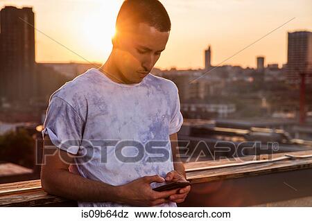 Young man looking at smartphone at sunset roof party in London, UK View Large Photo Image Stock Photo - Young man looking at smartphone at sunset roof party in London, UK. Fotosearch