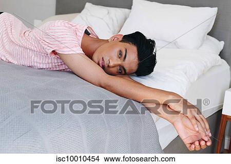 Picture - Young man lying on bed looking at camera, portrait. Fotosearch