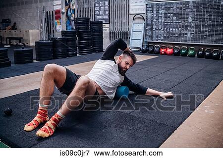 Young man massaging body with foam roller in gym View Large Photo Image Stock Photo - Young man massaging body with foam roller in gym. Fotosearch