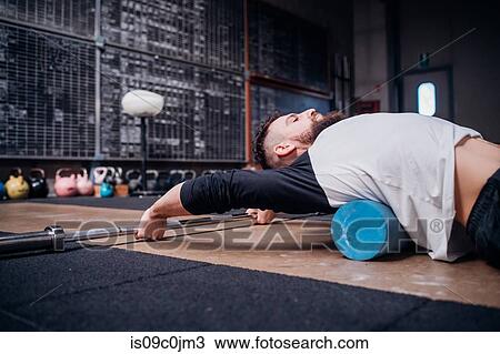 Young man massaging lower back with foam roller in gym View Large Photo Image Stock Image - Young man massaging lower back with foam roller in gym. Fotosearch