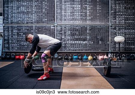 Stock Image - Young man placing weight plate into bar in gym. Fotosearch