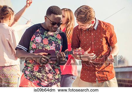 Young man playing ukulele at roof party in London, UK View Large Photo Image Picture - Young man playing ukulele at roof party in London, UK. Fotosearch