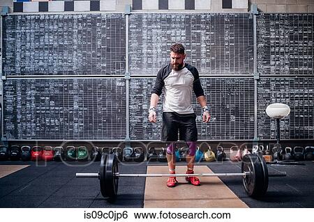 Young man preparing to lift barbell in gym View Large Photo Image Stock Photograph - Young man preparing to lift barbell in gym. Fotosearch