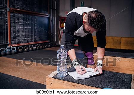 Stock Image - Young man reading checklist on notebook in gym. Fotosearch