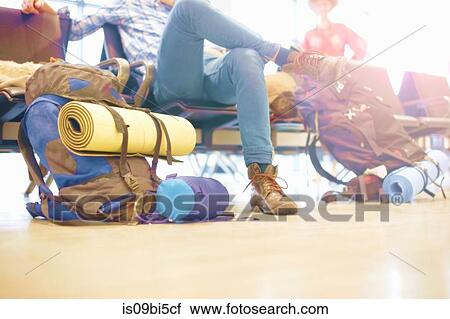 Stock Image - Young man sitting at airport, backpacks on floor beside him, low section. Fotosearch