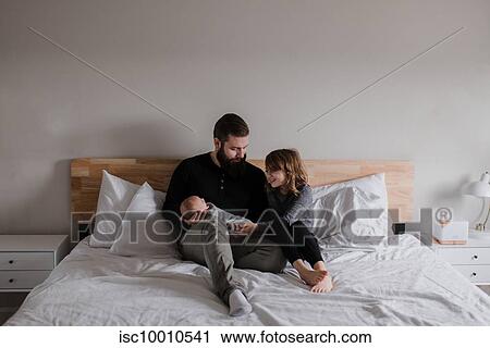 Young man sitting on bed with baby son and daughter View Large Photo Image Stock Image - Young man sitting on bed with baby son and daughter. Fotosearch