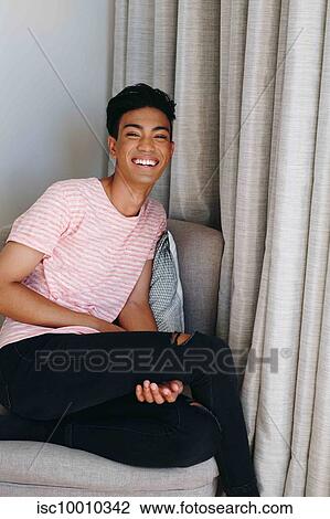 Young man sitting on bedroom chair laughing, portrait View Large Photo Image Stock Image - Young man sitting on bedroom chair laughing, portrait. Fotosearch
