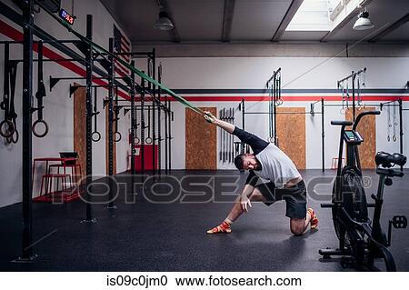 Young man stretching arm in gym View Large Photo Image Stock Image - Young man stretching arm in gym. Fotosearch