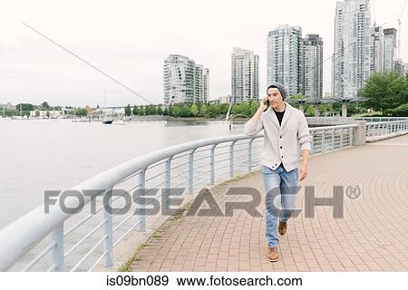 Young man talking on phone while walking along seawall, Yaletown, Vancouver, Canada View Large Photo Image Stock Photo - Young man talking on phone while walking along seawall, Yaletown, Vancouver, Canada. Fotosearch