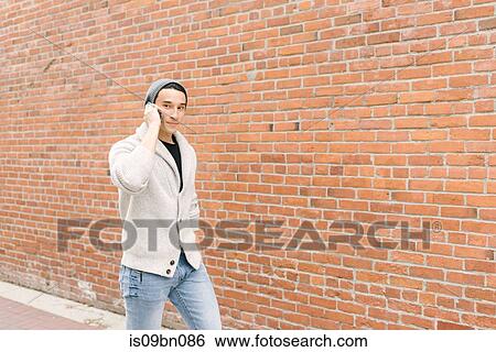 Young man talking on phone while walking along brick wall, Vancouver, Canada View Large Photo Image Stock Photograph - Young man talking on phone while walking along brick wall, Vancouver, Canada. Fotosearch