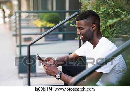 Picture - Young man using cellphone on step in streets of New York, US. Fotosearch