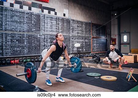 Young man watching woman lift barbell in gym View Large Photo Image Picture - Young man watching woman lift barbell in gym. Fotosearch
